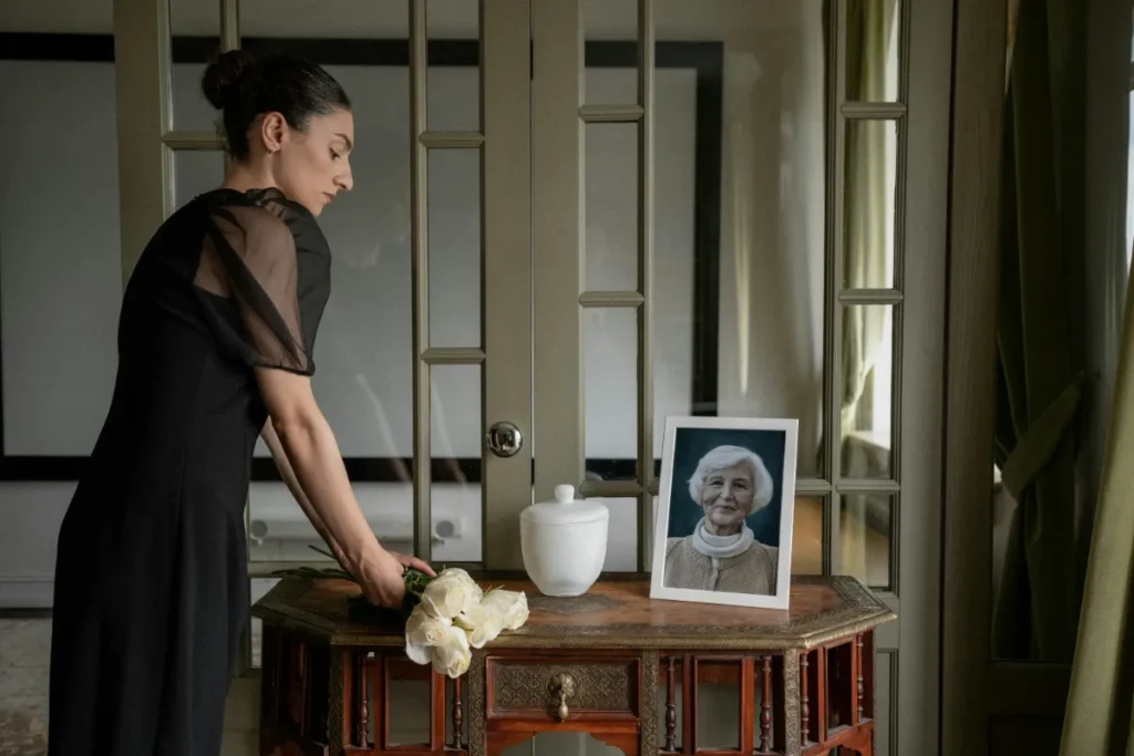 Mulher em luto coloca flores diante de urna funerária branca e retrato em homenagem.