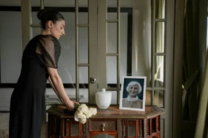 Mulher em luto coloca flores diante de urna funerária branca e retrato em homenagem.