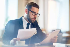 Advogado ou consultor de luto, de terno e barba, lendo atentamente documentos e papéis, representando a análise legal de patrimônio e o processo de inventário.