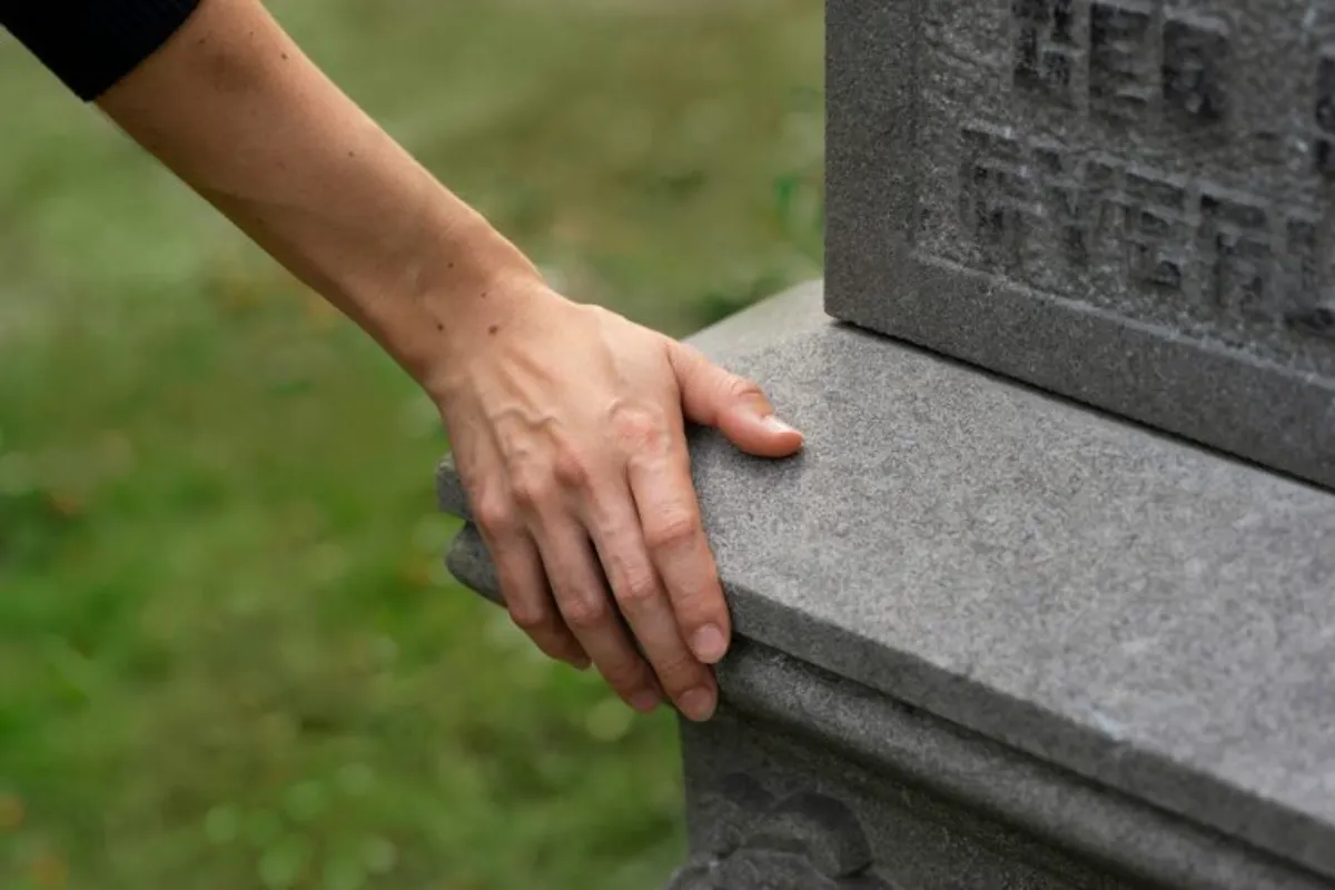 Mão apoiada em lápide de pedra em cemitério.